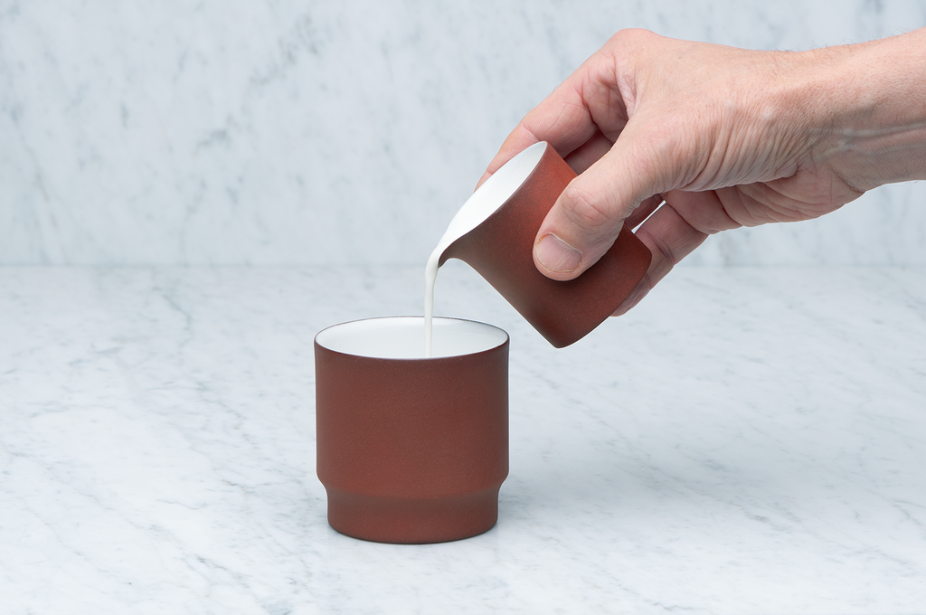 Brun och vit keramikkanna 0,7 dl som häller mjölk i en mugg