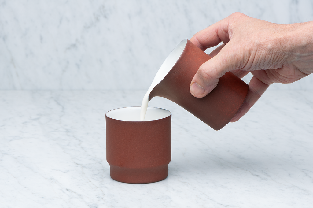 Brun och vit keramikkanna 2,5 dl som häller mjölk i en mugg