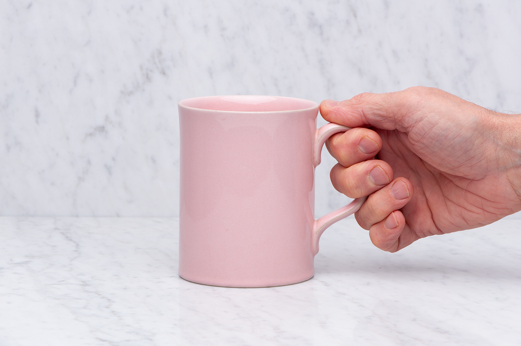 Ljusrosa temugg i keramik med hand som håller i handtaget. 5 dl