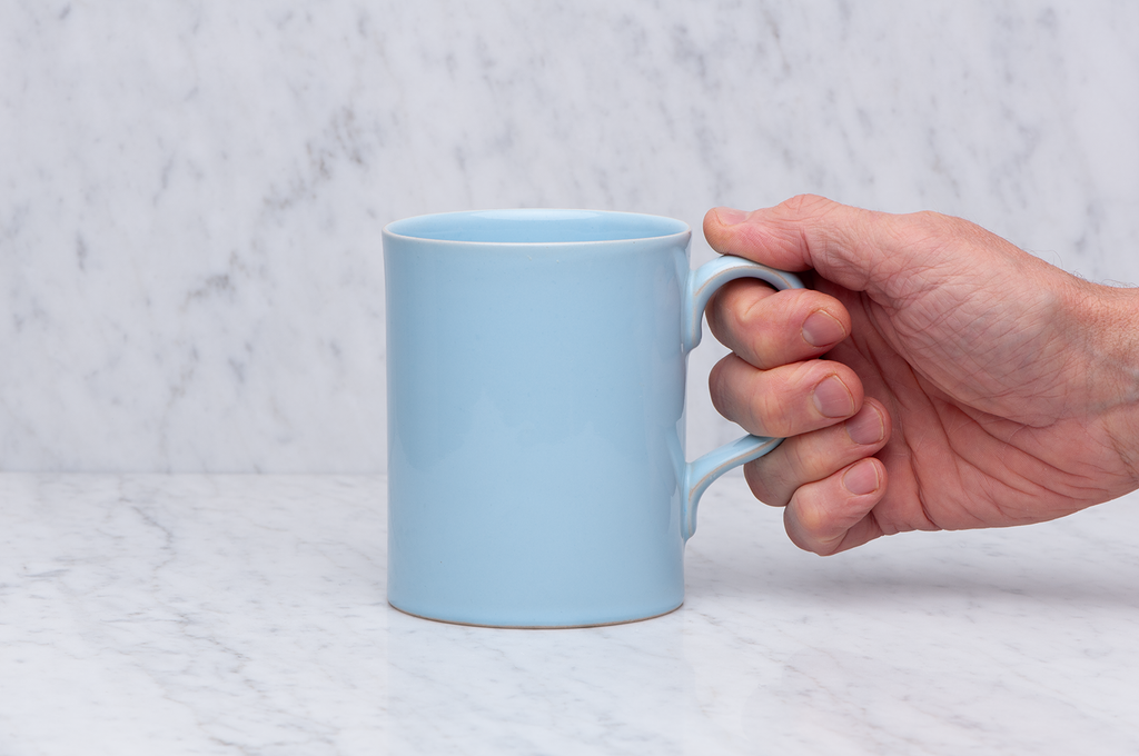 Ljusblå temugg i keramik med hand som håller i handtaget. 5 dl