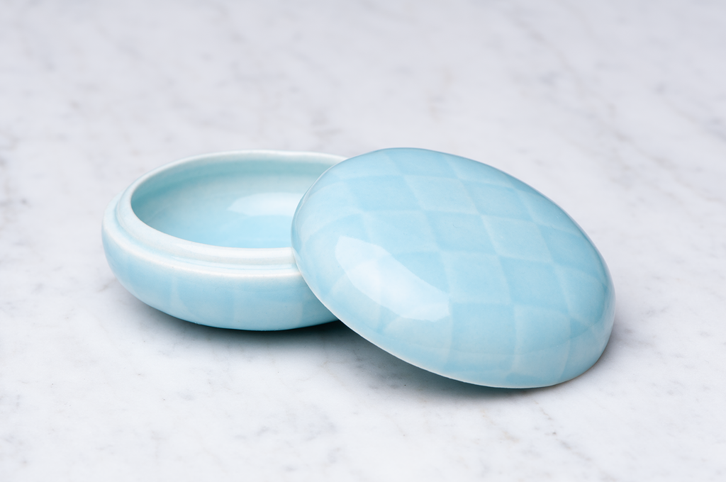 Ljusblårutig keramikask med locket på sidan.